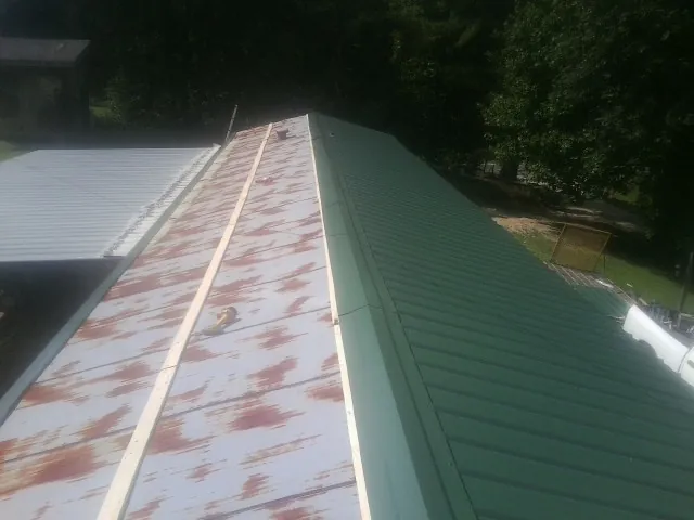 Old rusted panels beside newly installed green metal roofing — Wind Damage Roof Repair by Roofing Brothers in Henning