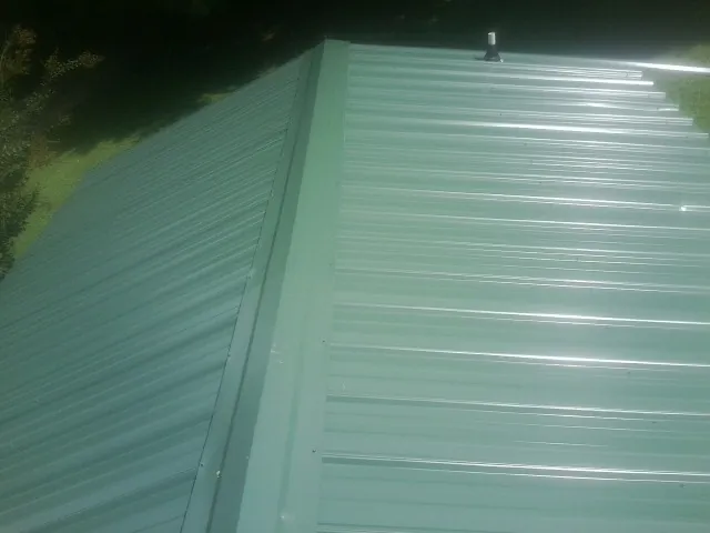New green metal panels meeting at the ridge of a roof — Flat Roof Repair work by our crew in Henning