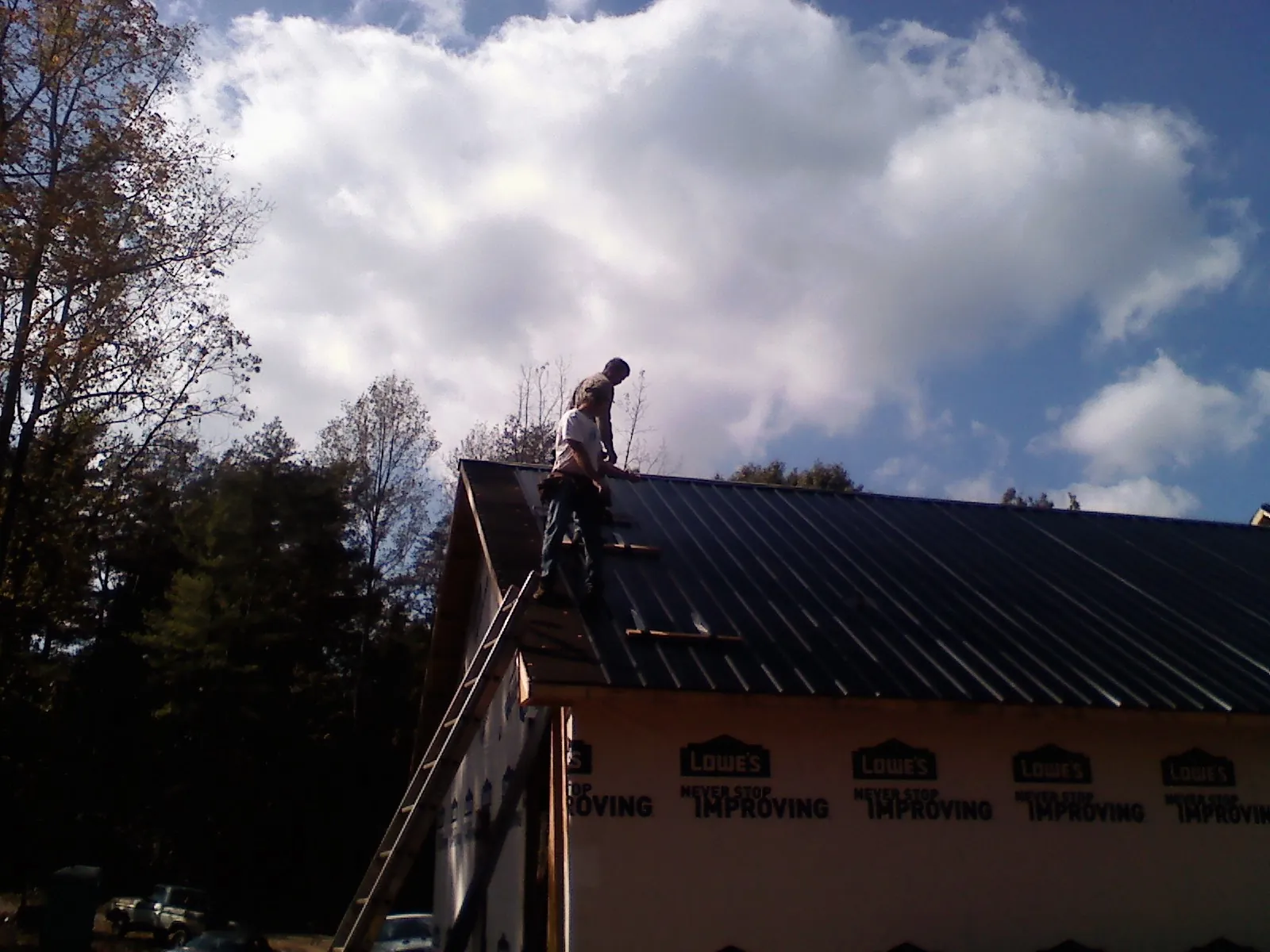Roofer fastening dark metal panels high against a cloudy sky, from a Roof Inspection job in Henning