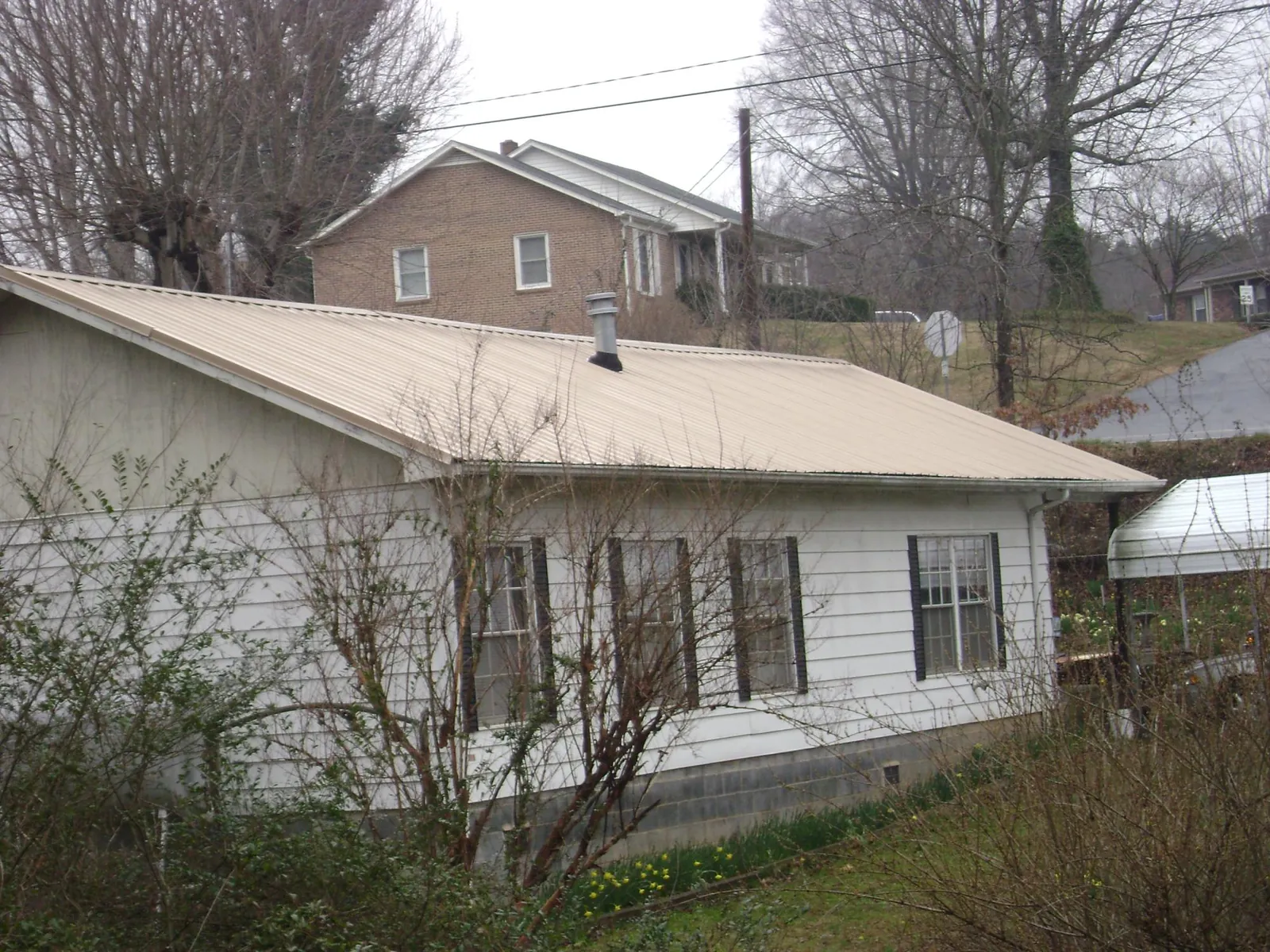 Tan metal roof on a white sided house set into a hillside — Commercial Roofing by Roofing Brothers in Henning