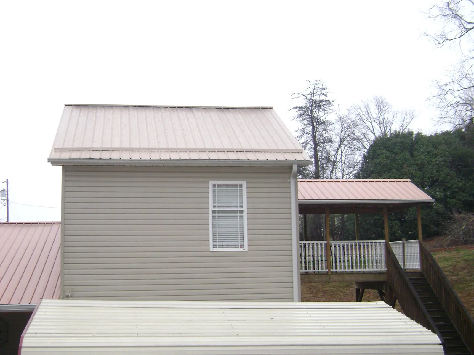 Tan metal roofs on a two story addition and attached porch, from a Roof Replacement job in Henning